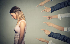 Concept of accusation guilty person girl. Side profile sad upset woman looking down many fingers pointing at her back isolated on grey office wall background. Human face expression emotion feeling