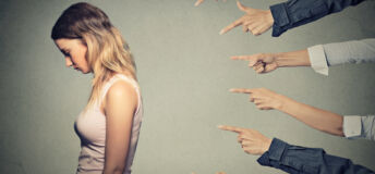 Concept of accusation guilty person girl. Side profile sad upset woman looking down many fingers pointing at her back isolated on grey office wall background. Human face expression emotion feeling