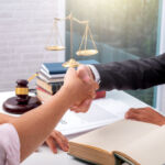 Image of business partners shaking hands with a legal scale in the background.