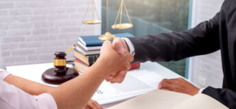 Image of business partners shaking hands with a legal scale in the background.