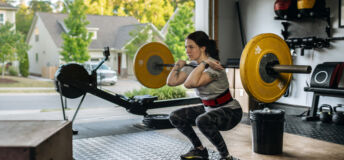 Photo of a fit woman performing a front squat with a heavy barbell in her home garage gym during covid-19 pandemic. Woman lifting a barbel and performing heavy powerlifting exercises. Power clean exercise. Focusing on core strength improvement.