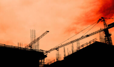 Residential building development and construction, back lit cranes and scaffold with orange sky