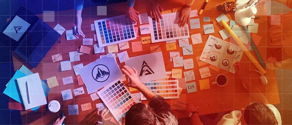 Marketing executives and graphic designers spread logo options and colour swatches over a table to decide on a rebrand