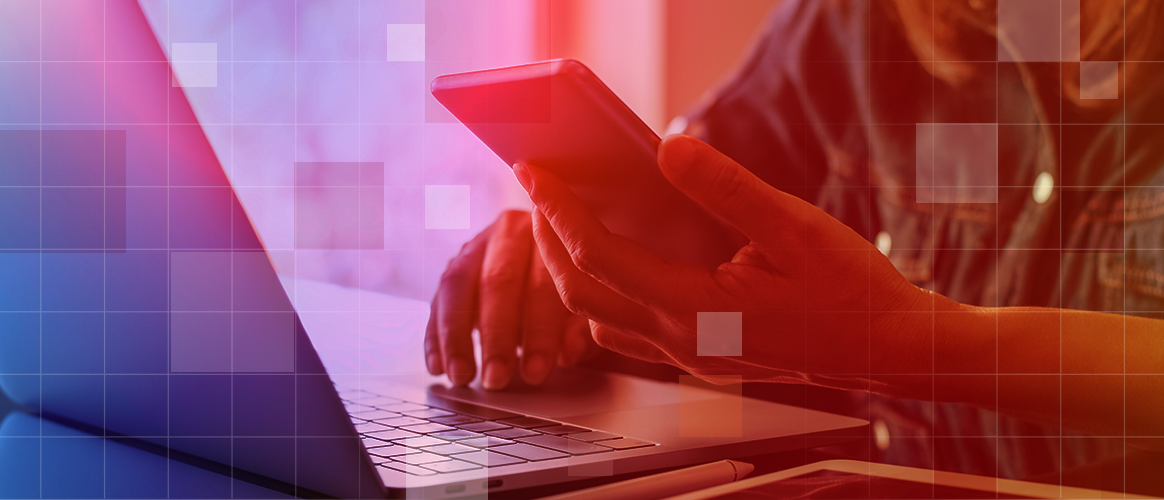 A person is reading their phone while sitting in front of a laptop