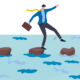 A businessman walks across stepping stones on water