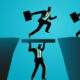 A businessman holds up a plank between two cliffs so other businessman can run over it