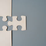 Two puzzle pieces connecting, one white and one grey, on a contrasting background